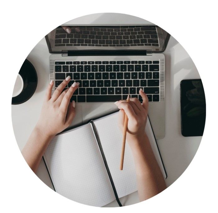 Hands typing on a laptop with a pencil and paper