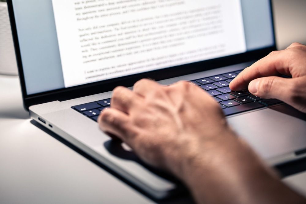 Hands typing on a laptop with text visible in the background